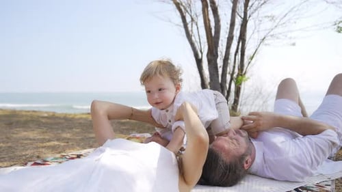4K Caucasian family resting together on blanket at the beach in summer sunny day.