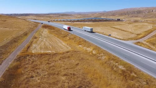 Truck drives on asphalt road along yellow fields and mountains. Aerial view.