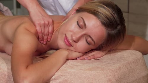Fröhliche Frau gönnt sich eine beruhigende Rückenmassage in einem ruhigen Spa
