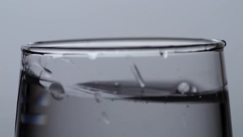 Primer plano del cubo de hielo que cae en un vaso de agua potable sobre el fondo de pantalla blanco claro
