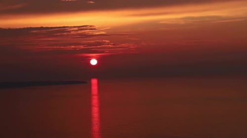 Lapso de tiempo al atardecer del sol rojo en el oceano/mar con movimiento de algunas nubes, 4k