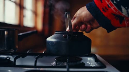 Person Boiling Water In A Tin Kettle On A Stovetop Inside Kitchen. Close-up Shot