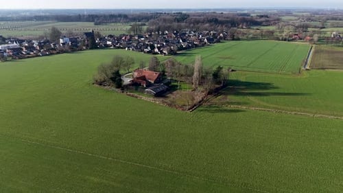 An expansive aerial drone shot of a traditional red roofed farmhouse nestled within square of trees