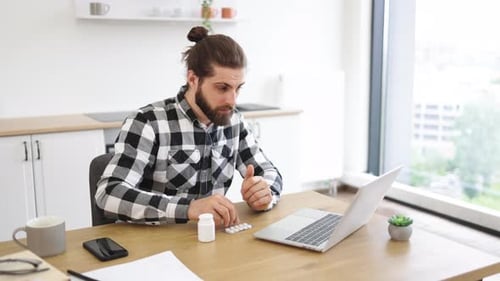 Feverish Bearded Man in Casual Clothes Touching Forehead While Looking at Laptop