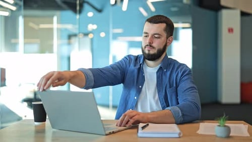 Man Closing Laptop at Office Desk