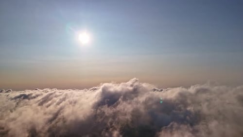 Aerial view of fluffy clouds with the sun shining brightly in clear sky above