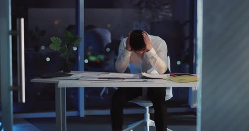 A Stressedout Professional is Working Late Into the Night in a Bustling Office Environment