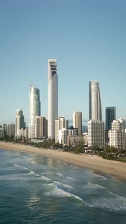 Vertical drone ocean waves rolling shore Gold Coast beachfront skyline high-rises Queensland view