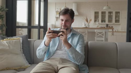 Young Man Plays Mobile Game on Couch