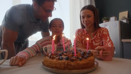 Girl Blowing Out Birthday Candles with Loving Family