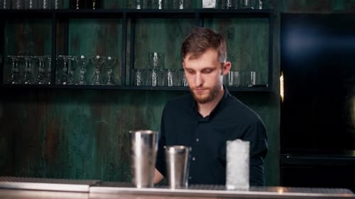 Male Bartender Hands Holding Bottle and Masterfully Pours Beverage Into Steel Jigger on a Black