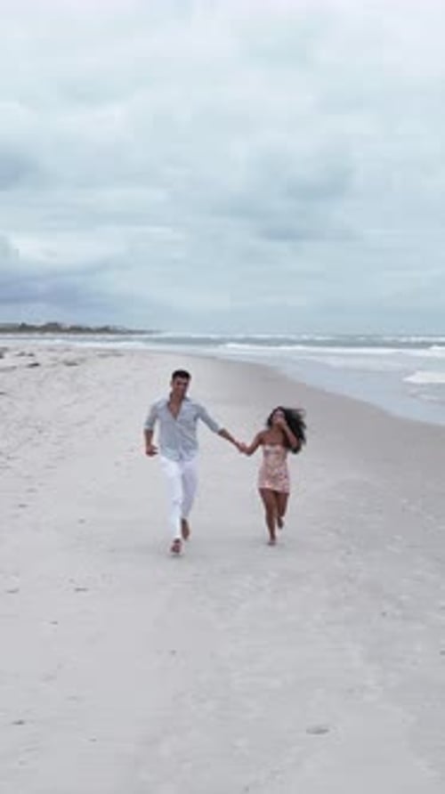 Romantic Interracial Couple Running Barefoot on the Beach Holding Hands