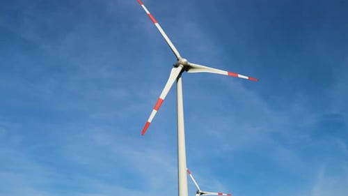 Low angle shot of wind turbines working and generating green electric energy in a wind farm under bl