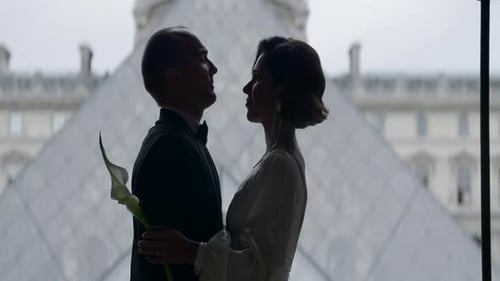 Casal feliz perto da pirâmide do museu do Louvre em Paris. Ação. Vista lateral do abraço da noiva e do noivo