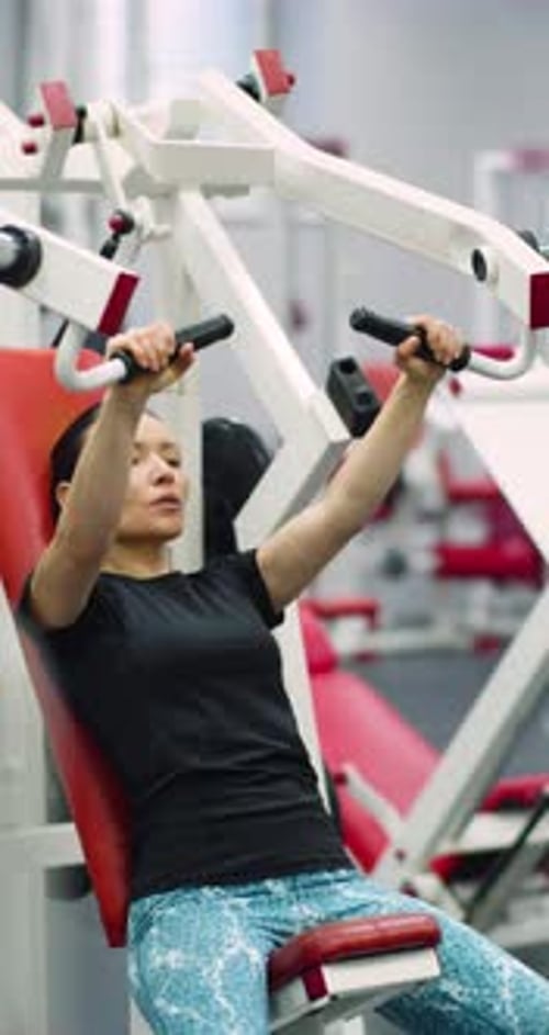Middleaged Woman Focused on Bench Pressing with the Hammer Machine at the Gym