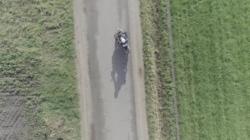 Drone shot motorcyclist driving on farm roads from above.