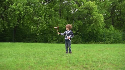 A Happy Boy in a Striped Shirt Creates Large Colorful Bubbles with a Bubble Wand in a Green Park The