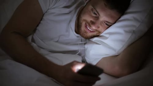 Smiling Man Using Smartphone in Bed at Night