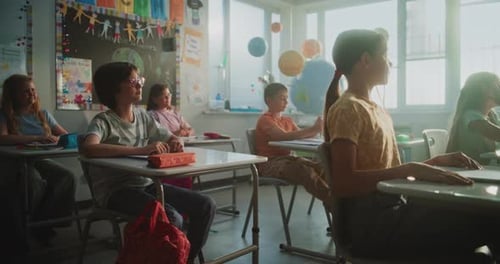 Primary School Children Sitting at the Desks Raising Hands to Give Correct Answer
