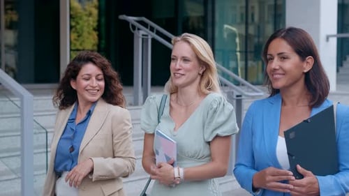 Smiling businesswomen walking together outside modern office.