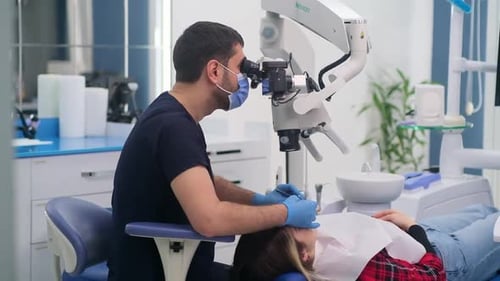 Dentist Working On Patient In Clinic Using Microscope