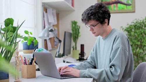 Young Male College Student Sitting at Desk at Home Using Laptop
