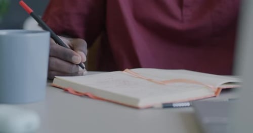 Closeup of Male Hand Writing with Pen in Paper Notebook Planning Office Work at Desk