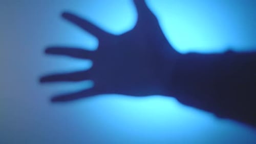 shadow play of hand making a fist in front of a blue wall