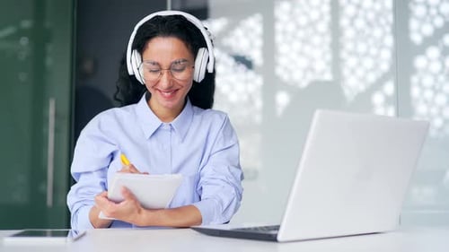 Smiling Woman Working at Laptop and Taking Notes