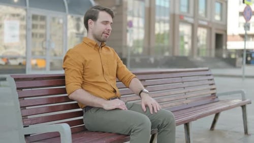 Man Sitting on Bench Rubbing His Back in Pain