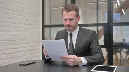 Worried Businessman Scrutinizing Corporate Documents in Office
