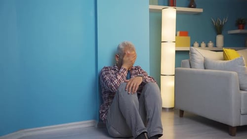 Man Sitting on Floor Against Wall Looking Sad
