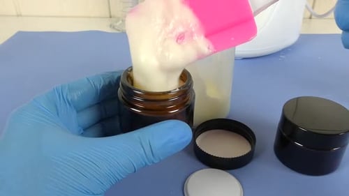 vue d'une scène de laboratoire de cosmétiques où un opérateur ganté utilise une spatule pour emballer soigneusement un sachet