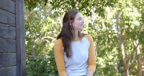 Femme adulte de 20 ans assise sur un banc se tournant vers la caméra au bon moment, les mains posées sur les genoux, souriant
