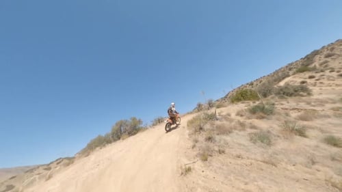 FPV high speed chase footage of motocross motorcycle riding along ridge, descending a little then tu