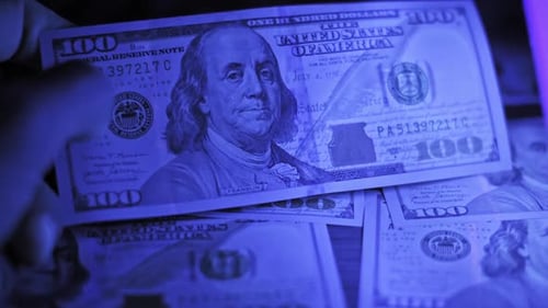 Examining US hundred dollar bills under a UV light