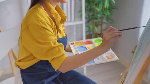 Asian young talented woman artist coloring on painting board in house.