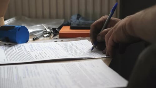Hand Filling Out Paperwork on Desk with Pen