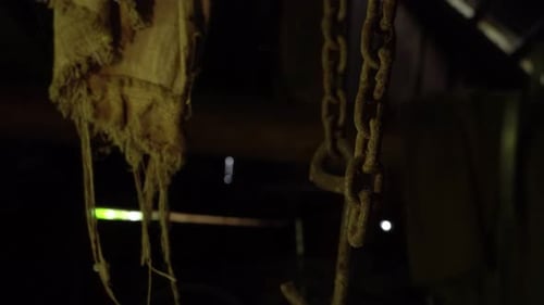Rusty chains hang from the ceiling and dangle in an abandoned basement, a metal chain and rusty
