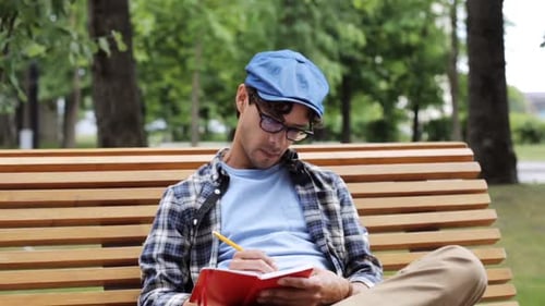 Man Sitting on Park Bench Writing in Notebook