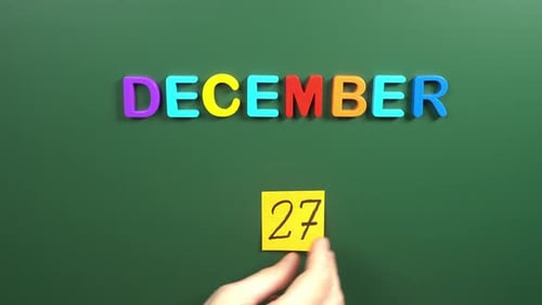 Hand sticking a sticker 27 December calendar day on school board. 27 date of December. Twenty