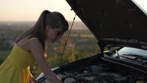 Puzzled Woman Driver Standing Near Her Car with Popped Up Hood Inspecting Broken Engine