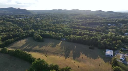 Hay bales on grass field of American countryside farm at sunset. Aerial wide shot. Peaceful nature