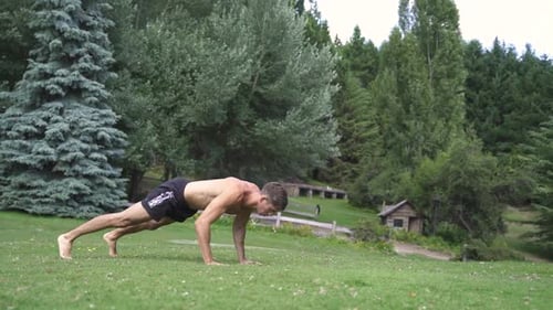 Young caucasian fit attractive male exersicing outdoors Burpees exercise with green vegetation backg
