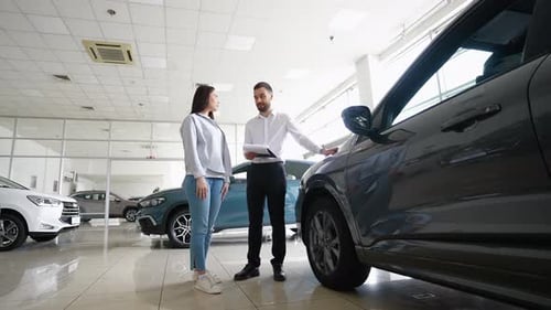 Salesperson in Car Showroom Showing a Car to Female Customer