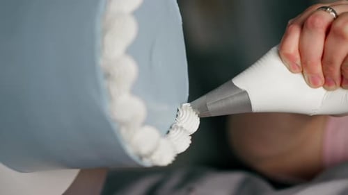 Vertical Video Closeup of a Female Baker in a Professional Kitchen Decorating Blue Cake with Cream