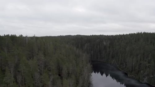 Drone flying over lake in the middle of forest a cloudy day.