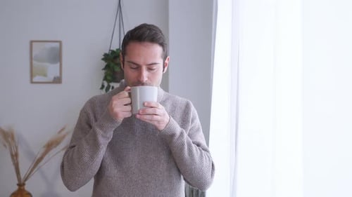 Young Adult Man Drinking Coffee By a Bright Window