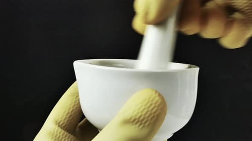 Des mains gantées travaillant avec précision avec un mortier en porcelaine, mettant en valeur la composition de formules dans un