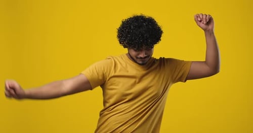 Young Indian Bearded Guy with Curly Hair Wearing Tshirt Dancing Over Orange Studio Background